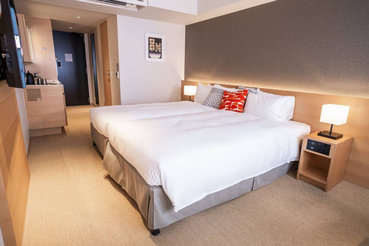 A hotel room with a large bed, bedside tables, a wardrobe, and a kitchenette area.