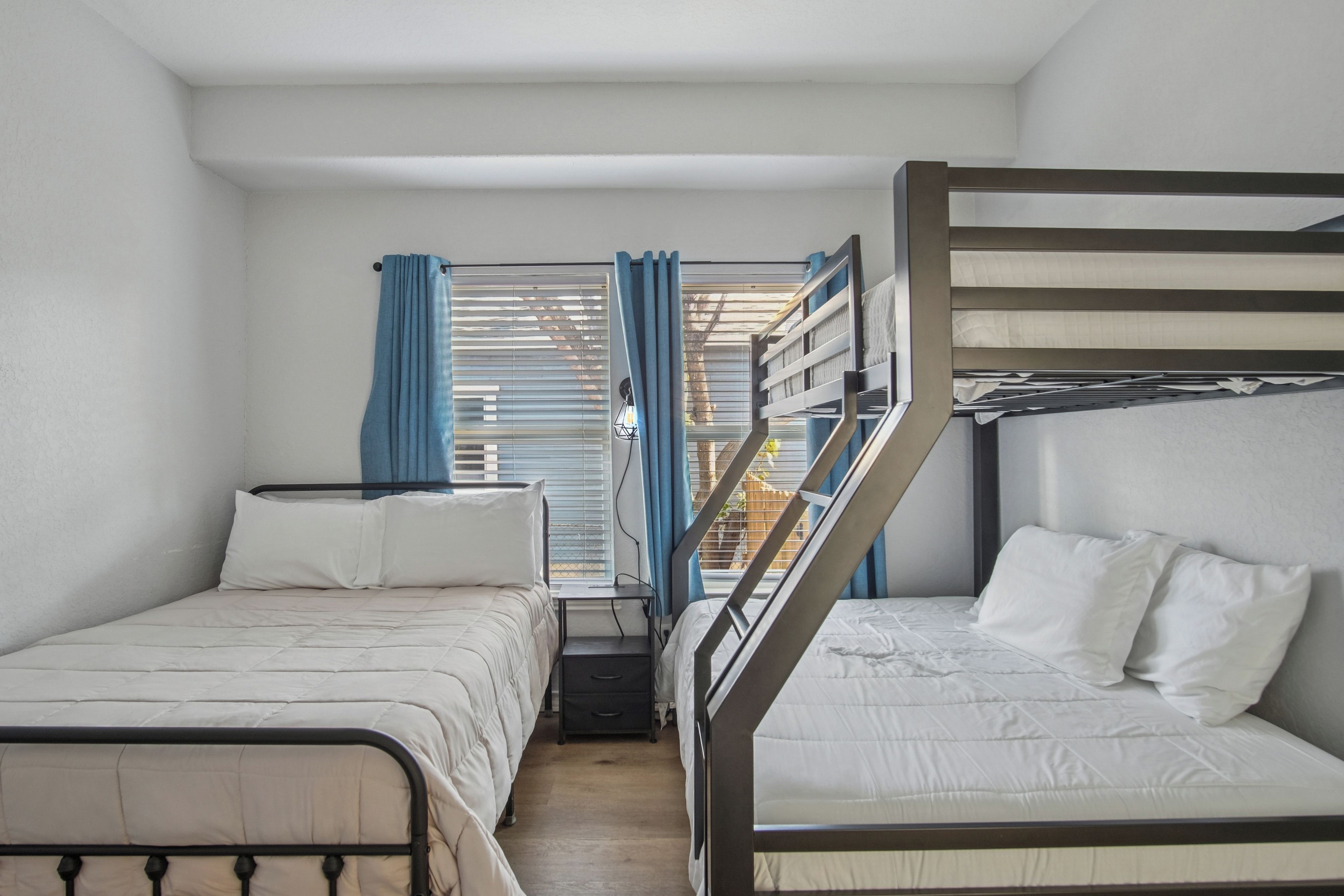 A room with two beds, a window with curtains, and a view of the outside.