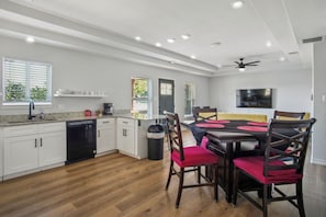 A modern kitchen with white cabinetry, a dishwasher, and a dining area with a table and chairs.