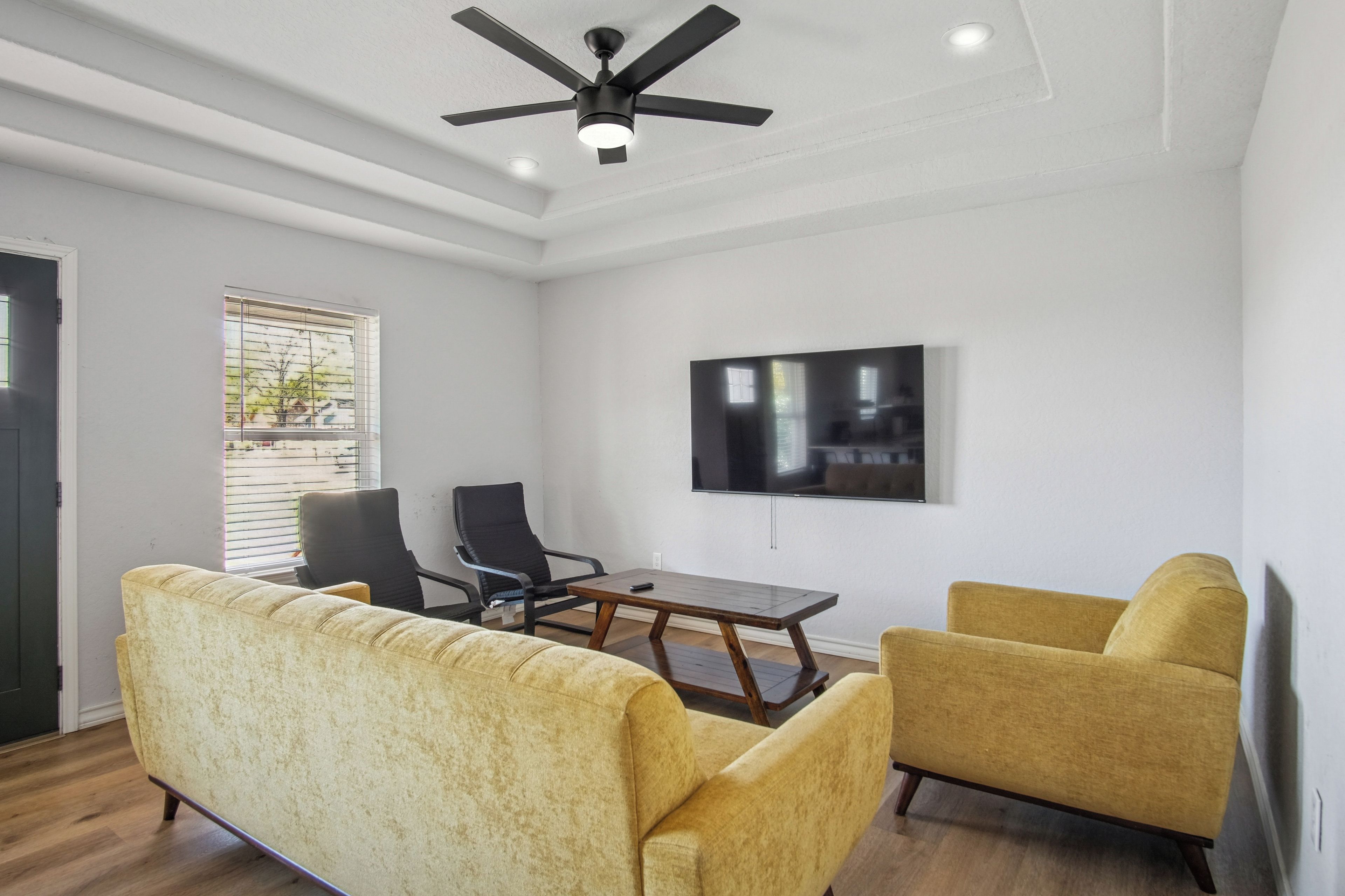 Sala de estar com ventilador de teto, TV de tela plana na parede e dois poltronas amarelas.