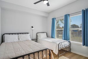 A bedroom with two beds, a ceiling fan, and a window with curtains.