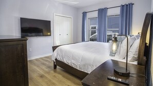 A bedroom with a bed, a TV mounted on the wall, a ceiling fan, and a bedside table with a lamp.