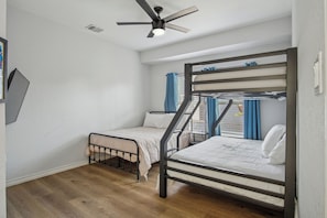A room with a bunk bed, a single bed, a ceiling fan, and a window with curtains. - Cozy Downtown Oasis! (San Antonio)