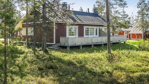 Une cabane dotée d’une terrasse en bois, entourée d’arbres et d’une zone herbeuse.