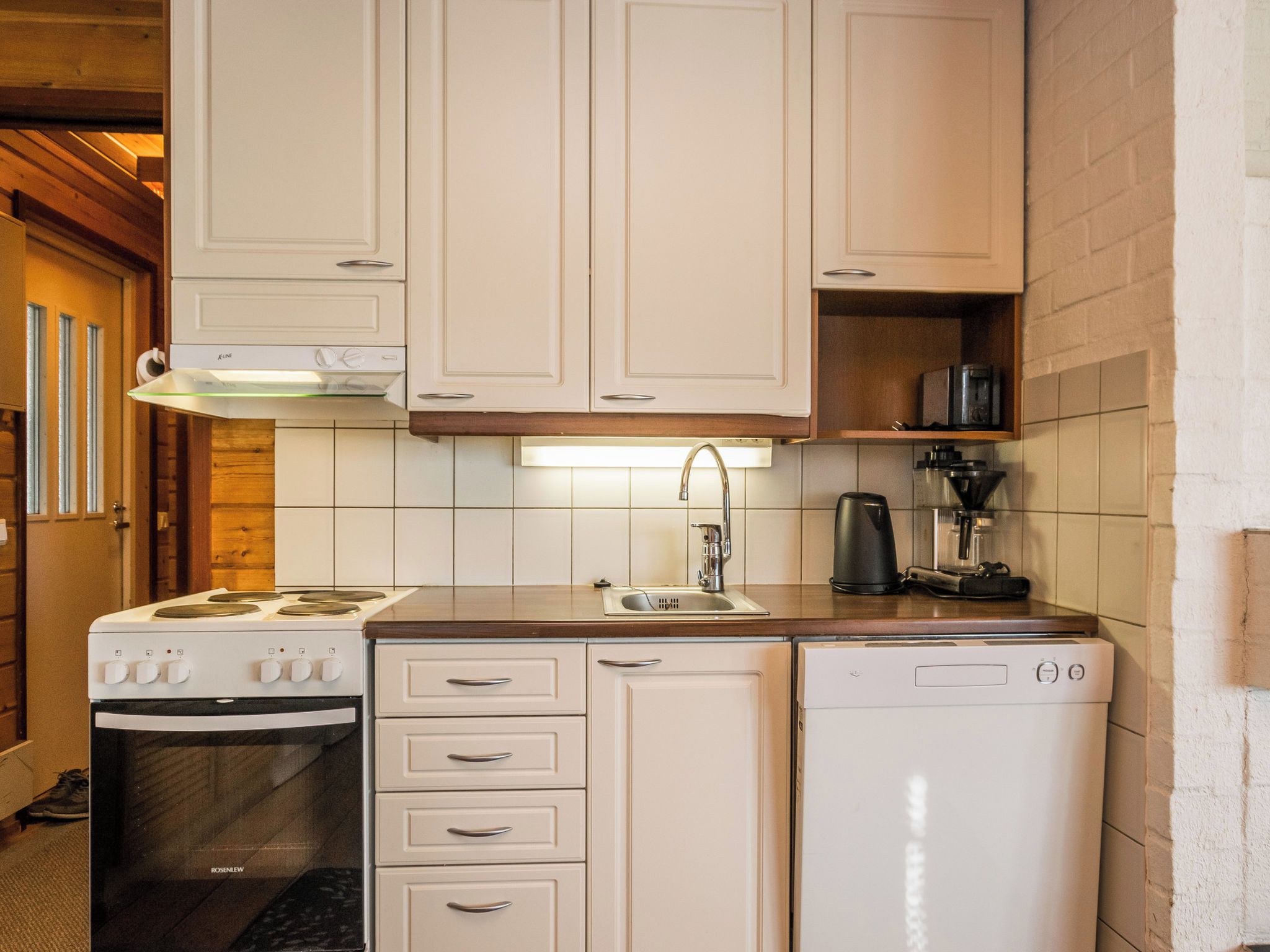 Een compacte keuken met witte kastjes, een ingebouwde oven, een vaatwasser en een koffiezetapparaat.