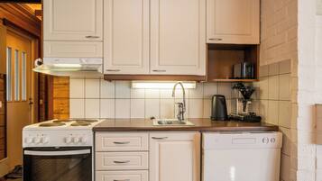 Een compacte keuken met witte kastjes, een ingebouwde oven, een vaatwasser en een koffiezetapparaat.