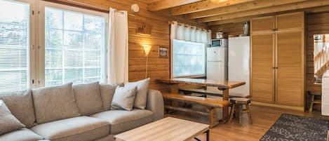 Interior de una cabaña de madera con sofá, mesa de comedor y zona de cocina.