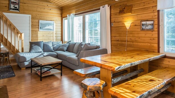 L’intérieur chaleureux d’un chalet, avec un revêtement mural en bois, un canapé, une table à manger et un escalier.