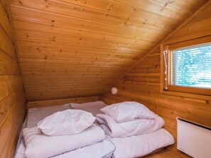 A small, wooden cabin room with a single bed, a window, and a white heater.
