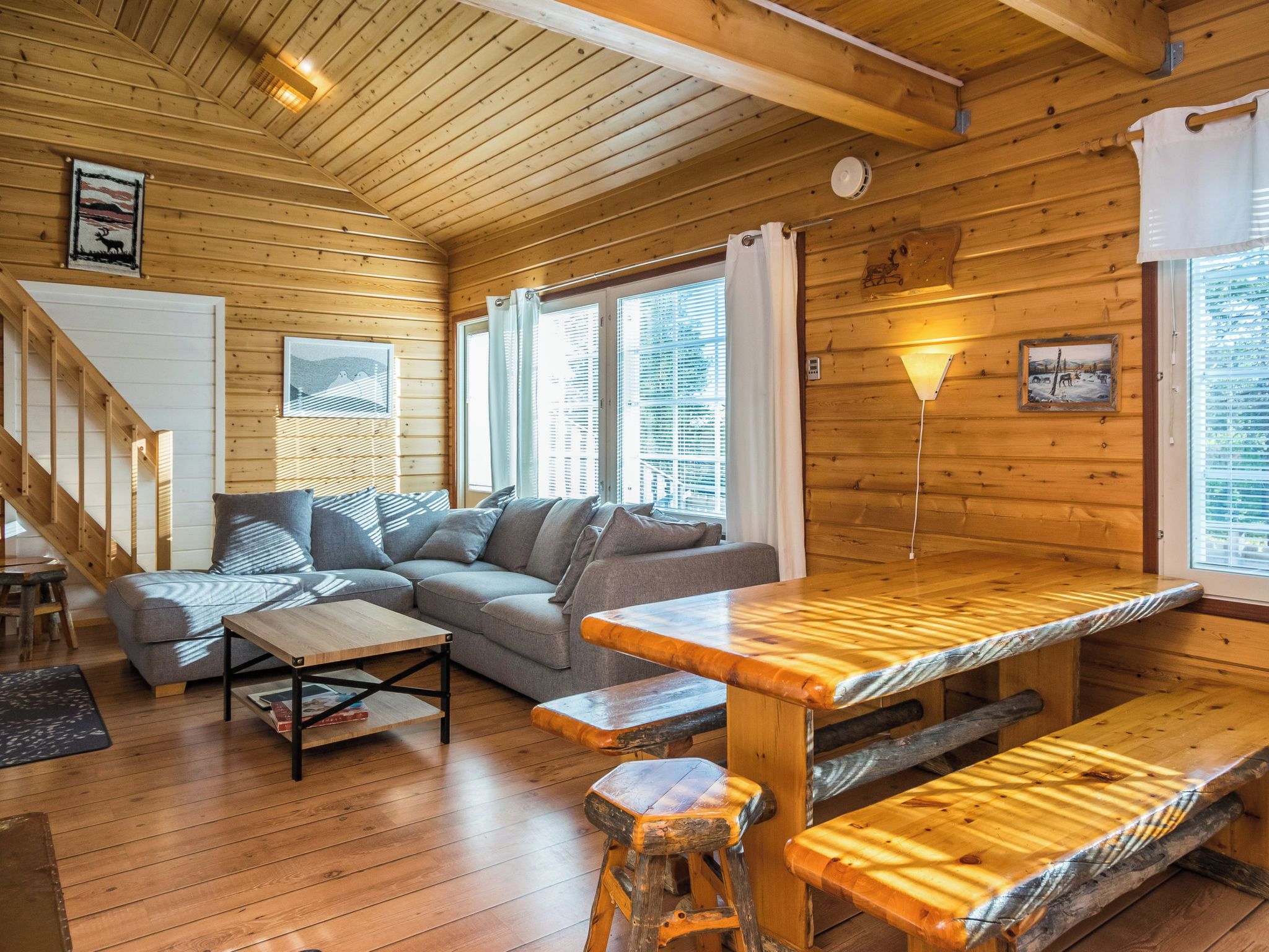 Ein gemütliches Blockhauskamin mit Holzboden, einer Couch, einem Esstisch und einer Treppe.