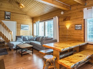 Een gezellig blokhutinterieur met een houten vloer, een bank, een eettafel en een trap.