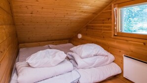 Une petite pièce en bois, aménagée comme une cabane, avec un lit simple, une fenêtre et un radiateur blanc.