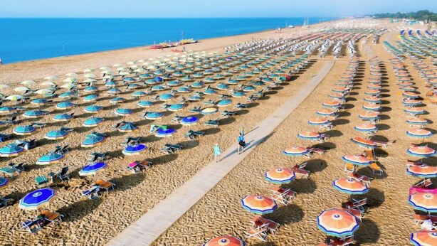 Une plage bordée de rangées de parasols et de chaises, un ciel dégagé et l’océan en toile de fond.
