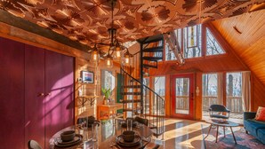 A spacious loft with a high ceiling, a dining area with a glass table, and a cozy seating area with a blue sofa. - Firepit + Mountain Views | A-Frame in Fairview | Honeycomb Hideaway by AvantStay (Fairview)