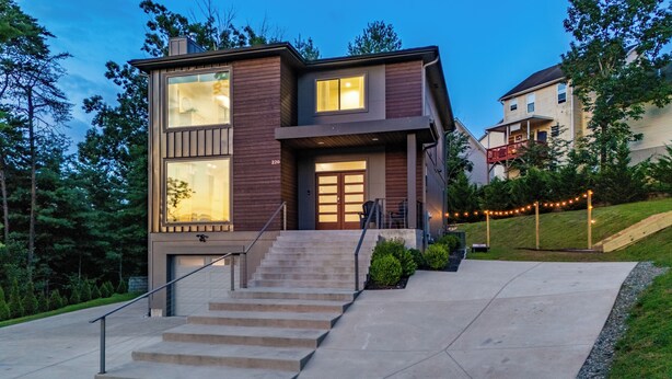A modern two-story house with a staircase leading to the front door, surrounded by greenery and a well-maintained lawn. - Hot Tub, Fire Pit, Mountain Views, 10min to AVL |  Modern Escape by Avanstay (Asheville)