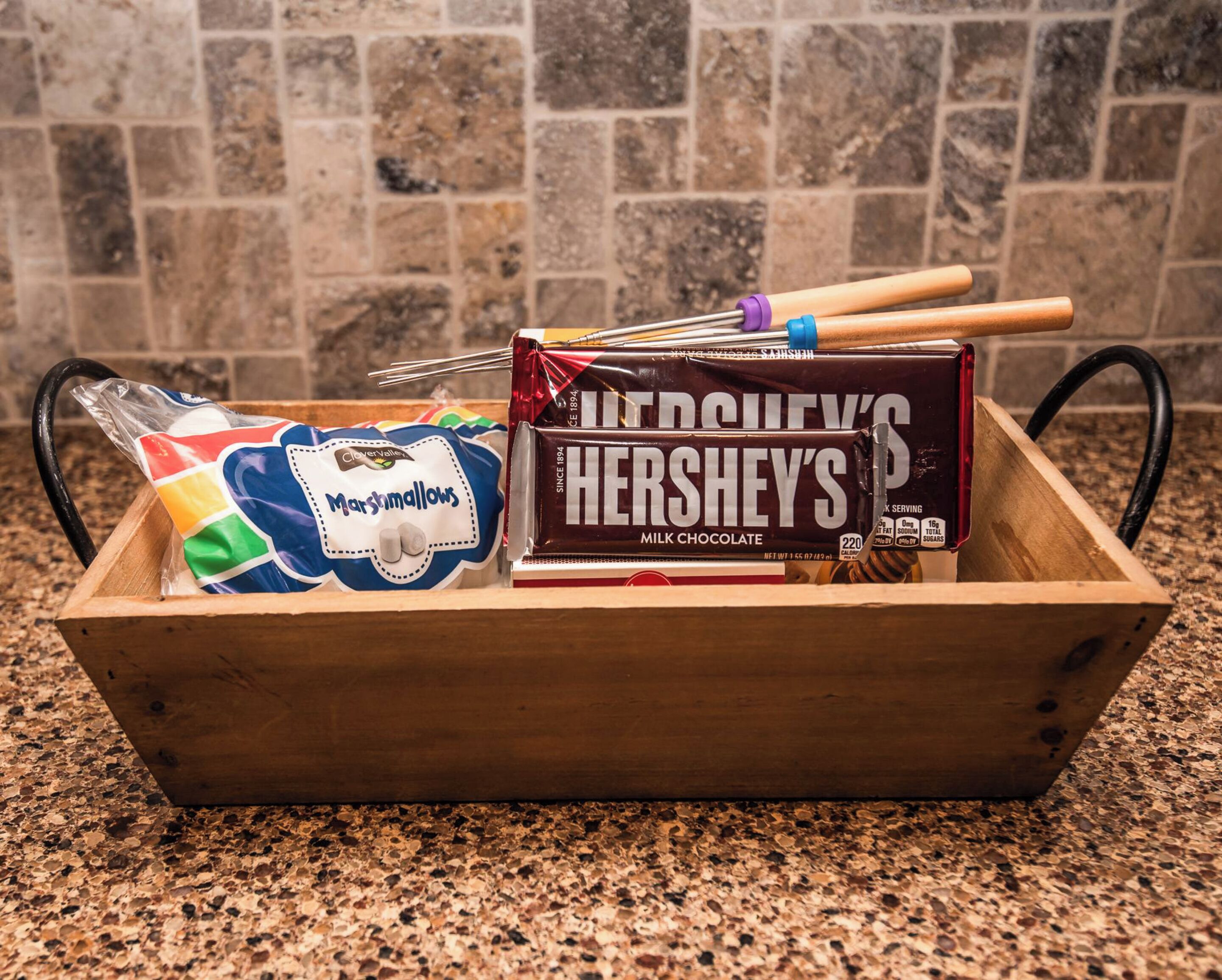 A wooden box containing a Hershey's Milk Chocolate bar, a bag of marshmallows, and a colorful marshmallow-themed item.