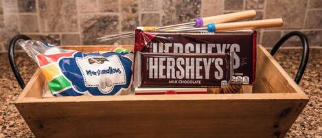 A wooden box containing a Hershey's Milk Chocolate bar, a bag of marshmallows, and a colorful marshmallow-themed item.