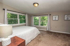 A bedroom with a bed, a nightstand, a lamp, and two windows with curtains.