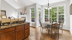 Una cocina con encimera de granito, armarios de madera, pileta doble y una zona de comedor con mesa y sillas.