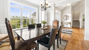 Un comedor con una mesa grande, sillas, una araña y vistas al exterior.