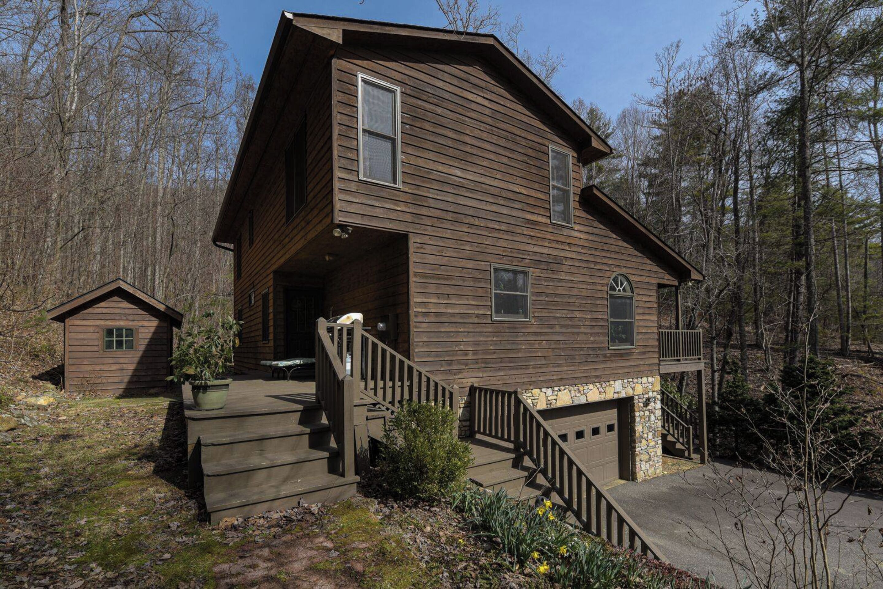 A two-story wooden cabin with a stone foundation, a front porch, and a small attached shed.