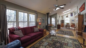 A spacious living room with a red sofa, wooden flooring, and large windows. - Creekside Mountain by AvantStay | Private Sauna (Asheville)