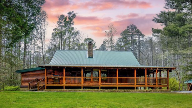 A log cabin with a green metal roof, wooden deck, and a chimney.