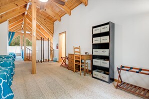 Ein Zimmer mit Holzbalkendecke, einem Schreibtisch mit Schubladen, einem Stuhl, einer Bank und Aufbewahrungsboxen an der Wand.