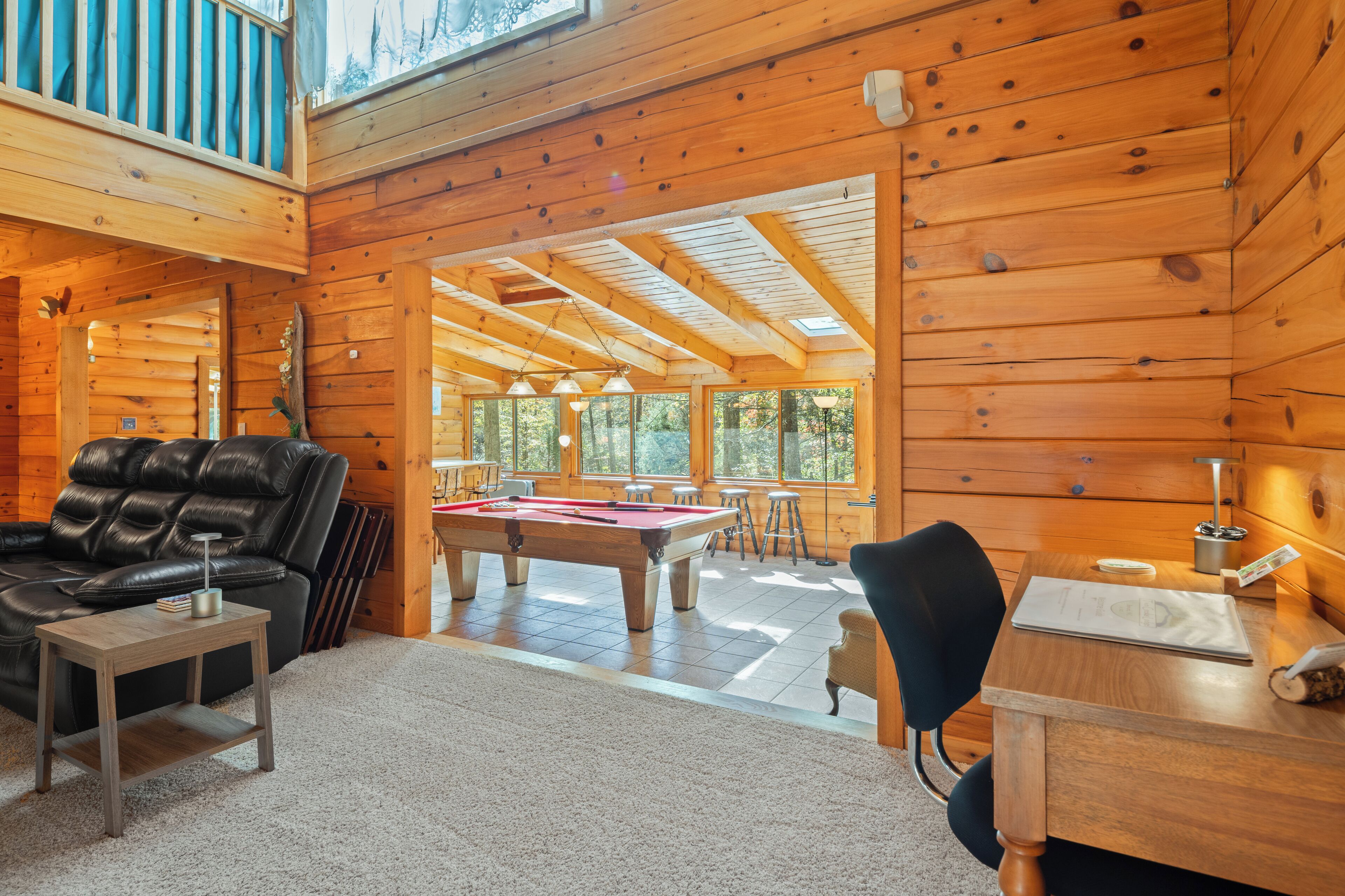 L’intérieur d’un chalet en bois chaleureux et accueillant, avec une table de billard, un canapé en cuir et un coin repas baigné de lumière naturelle.