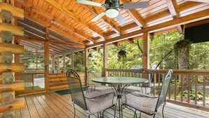 A wooden deck with a table and chairs, surrounded by glass doors and windows, overlooking a forested area.