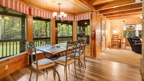 A wooden cabin interior with a dining table, chairs, and a view of the forest.
