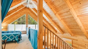 A wooden cabin with a loft bedroom, a balcony, and a view of the outdoors.