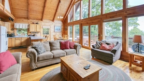 A spacious cabin interior with a wooden ceiling, large windows, a kitchen area, and a living room furnished with sofas and a coffee table. - Incredible View, Hot Tub, Fire Pit, Grill & Foosball | Mountain Gem by AvantStay (Waynesville)