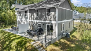 A two-story house with a patio area featuring a table and chairs, a covered grill, and a stone staircase leading to the entrance. - Little Sycamore by AvantStay | Premier Location + Patio | Sycamore Cove Gem (Asheville)