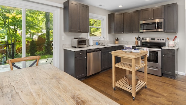 A modern kitchen with dark cabinets, stainless steel appliances, and a wooden table. - Little Sycamore by AvantStay | Premier Location + Patio | Sycamore Cove Gem (Asheville)