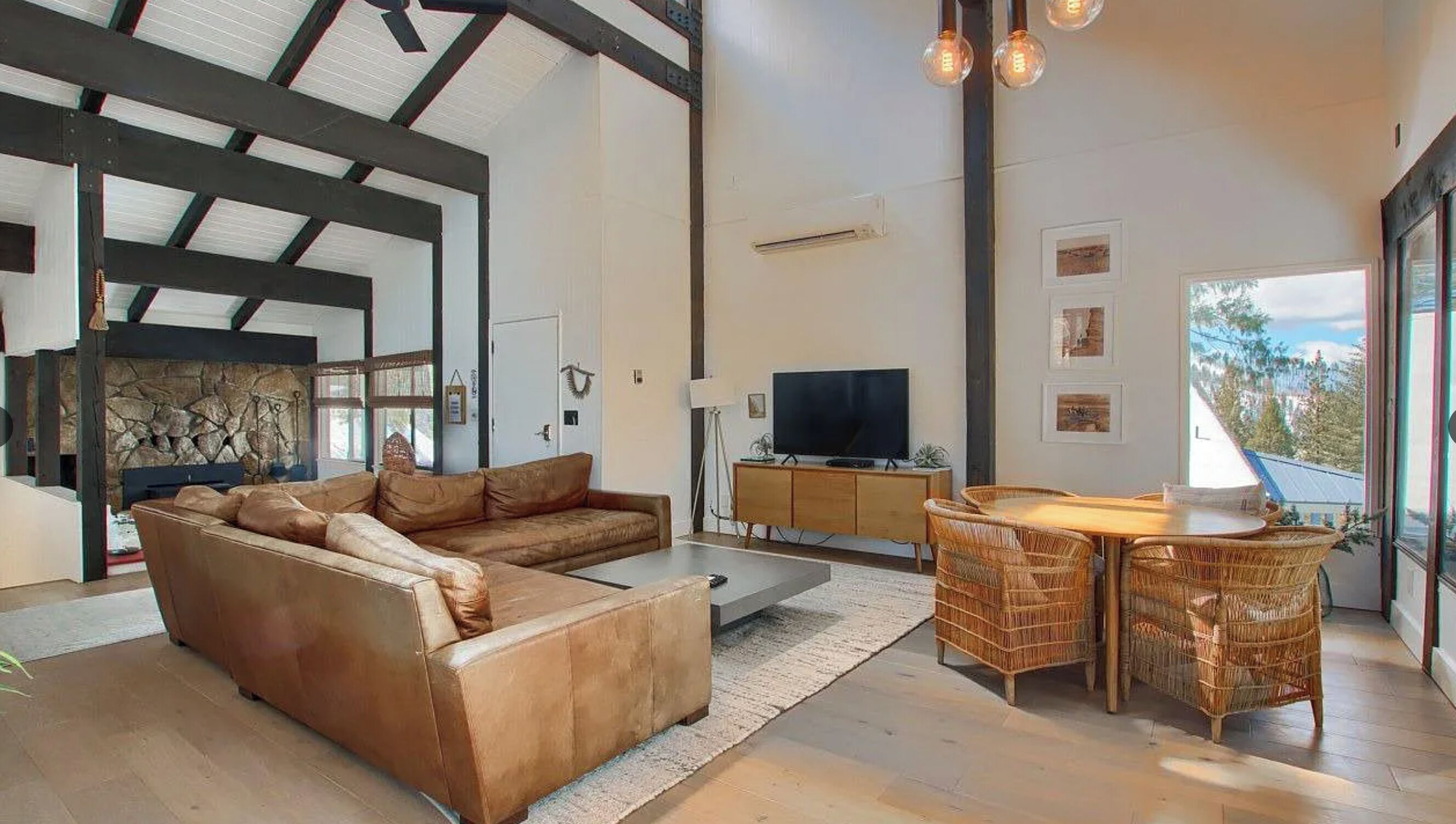 A spacious living area with a sectional sofa, a dining table with chairs, a flat-screen TV, and a stone fireplace.