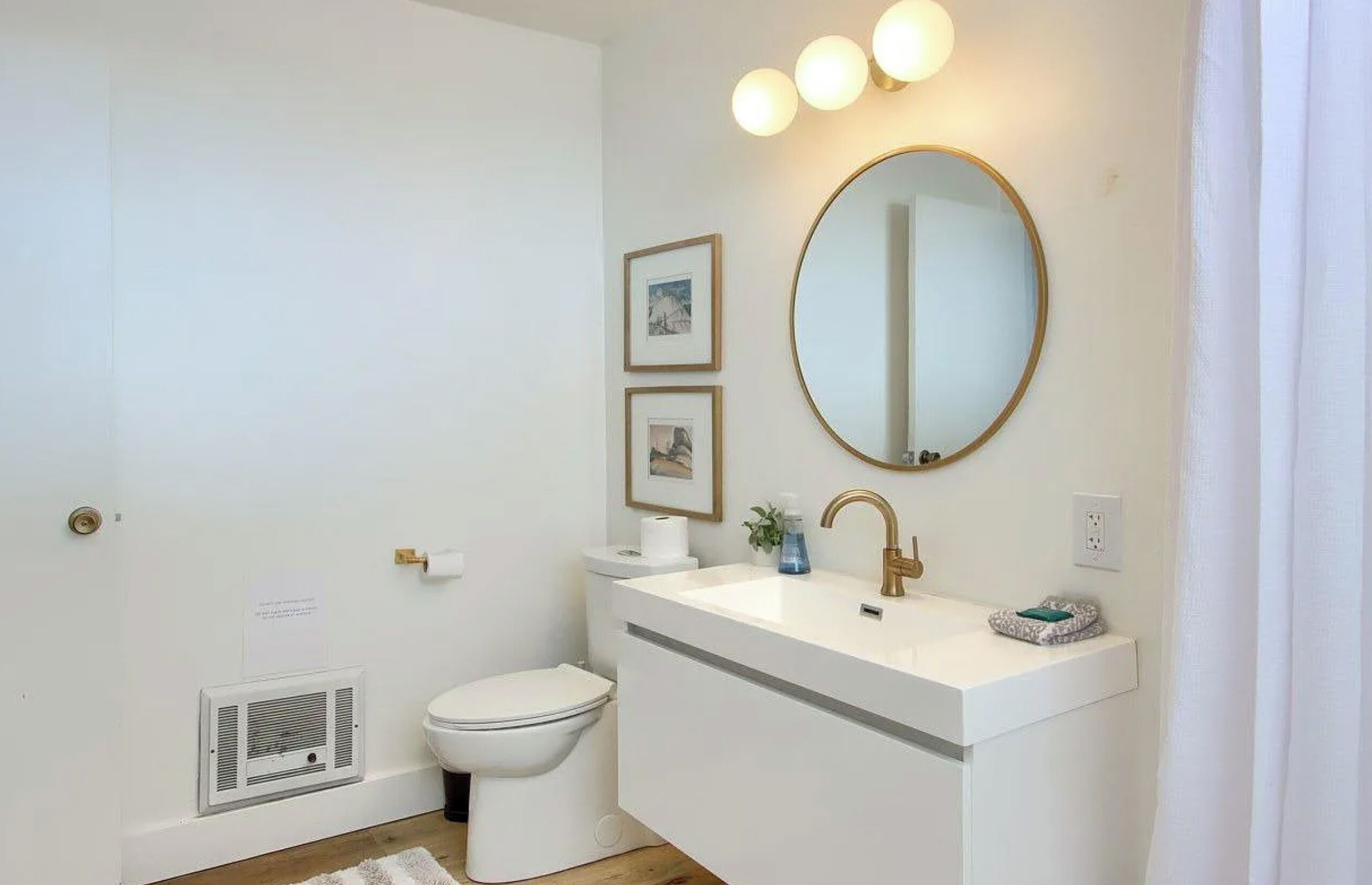 Une salle de bain moderne avec un lavabo blanc, un robinet doré et un miroir rond.