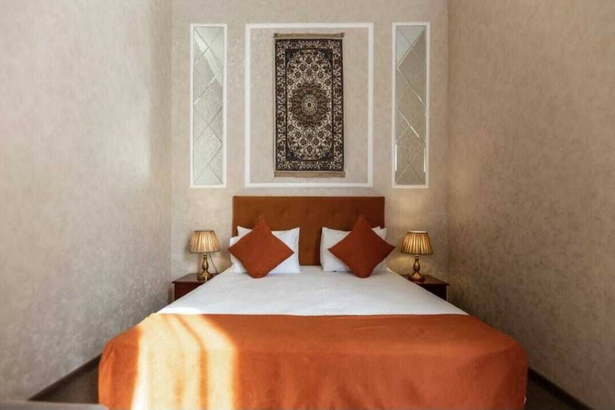 Une chambre d’hôtel avec un grand lit, deux lampes de chevet, une tapisserie à motifs sur le mur et une tête de lit marron.