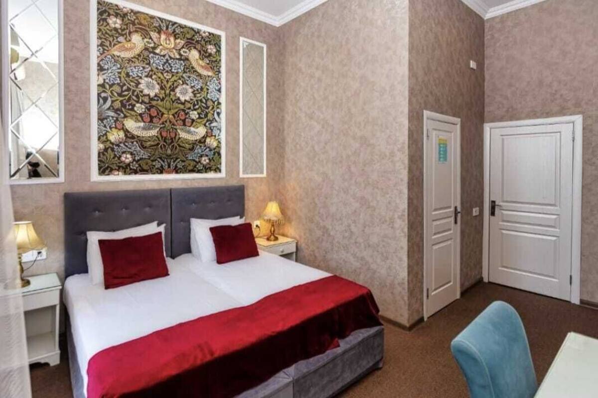 Une chambre d’hôtel avec un grand lit, deux tables de chevet avec des lampes, un plaid rouge, une chaise bleue et un élément décoratif mural.