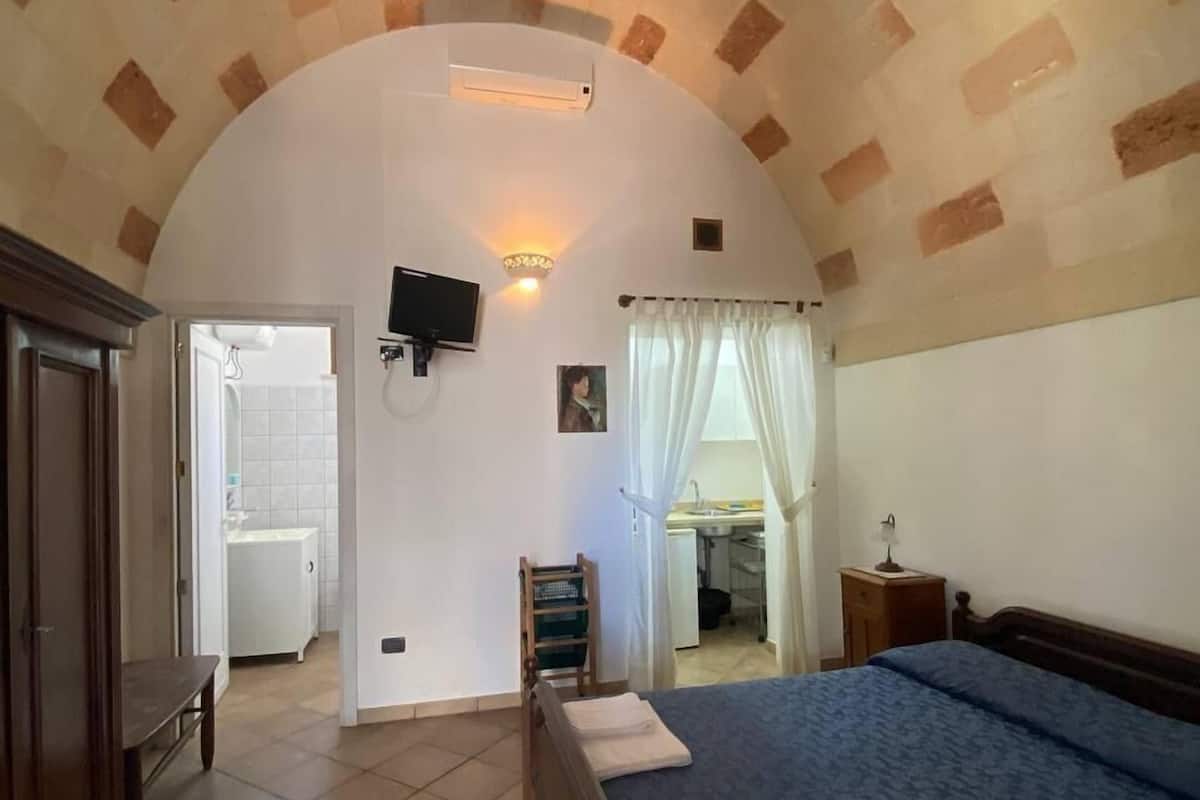 Un dormitorio con una cama grande, un armario de madera, un escritorio con lámpara y un televisor montado en la pared.