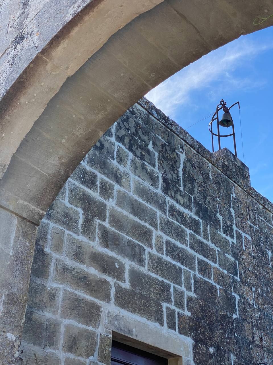 A stone wall with a metal bell tower.
