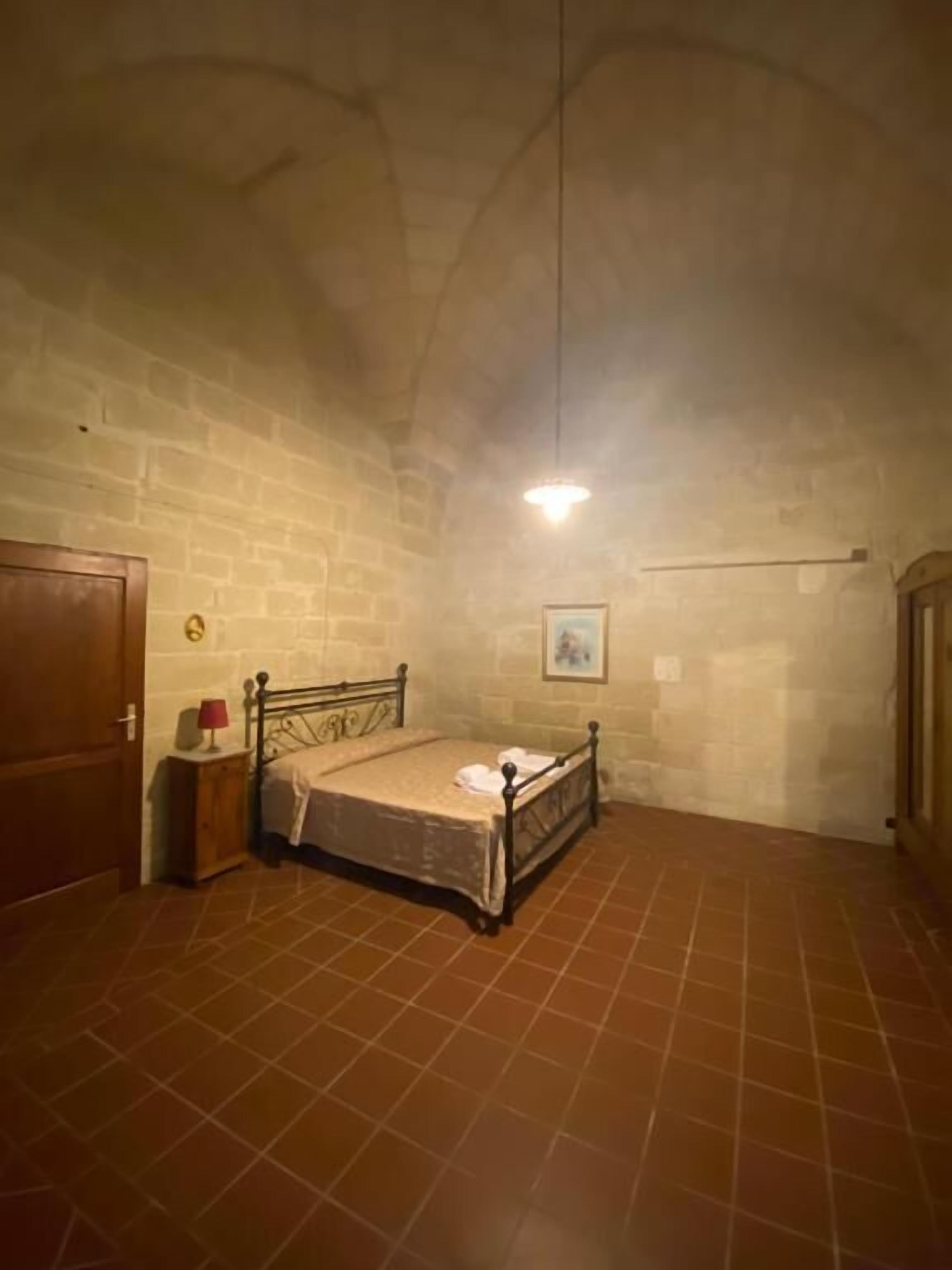 Een slaapkamer met een bed, nachtkastje, lamp en een foto aan de muur.