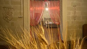An arched doorway with red curtains, a bed with a headboard, and wheat stalks in the foreground.