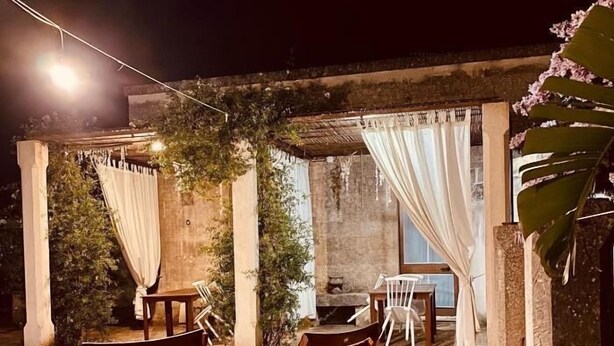An outdoor patio area with stone flooring, wooden chairs, a table, and a hanging light.