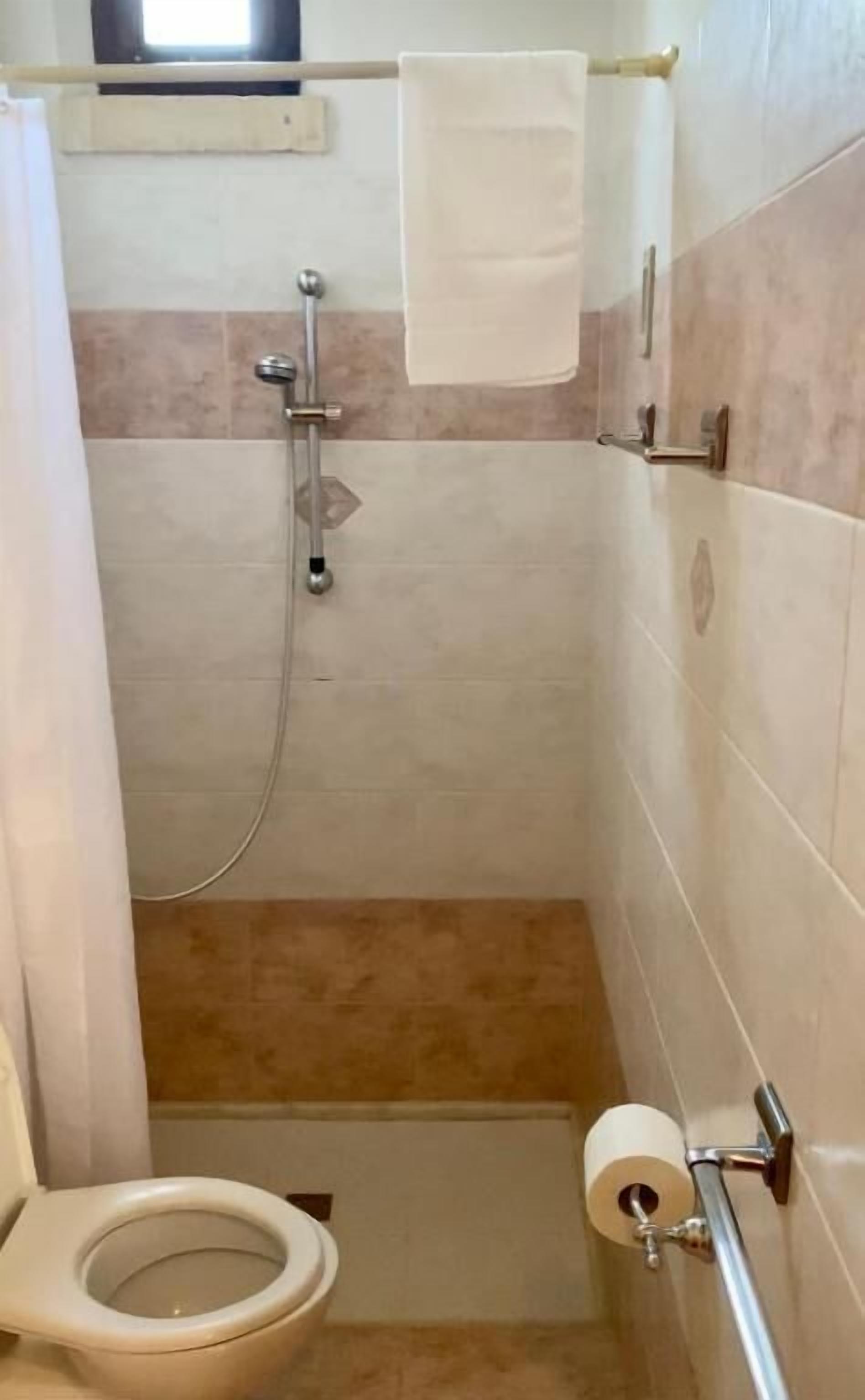 A small, narrow bathroom with a shower, toilet, and a towel rack.