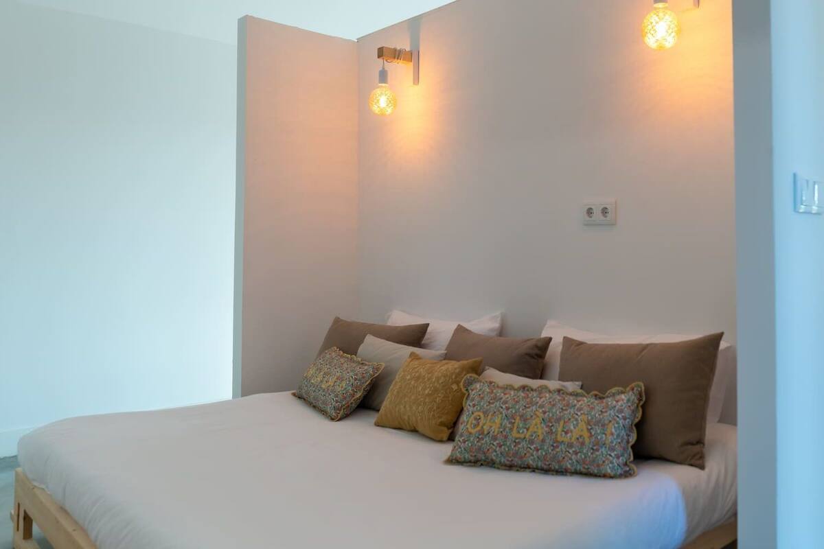 A bedroom with a bed, pillows, and wall-mounted lights.