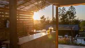 A wooden bar area with a view of the sunset, outdoor seating, and a pergola structure.