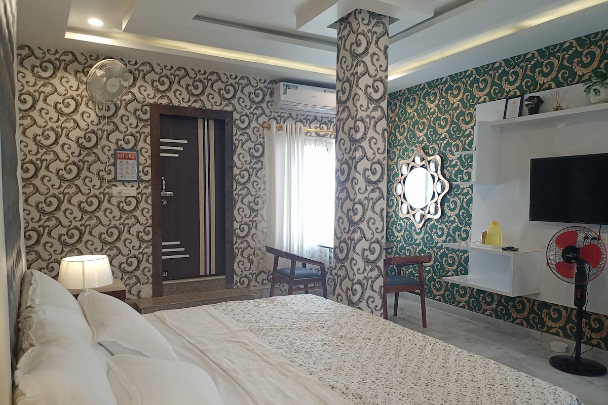 A hotel room with a bed, a desk, a chair, a TV, and a fan.