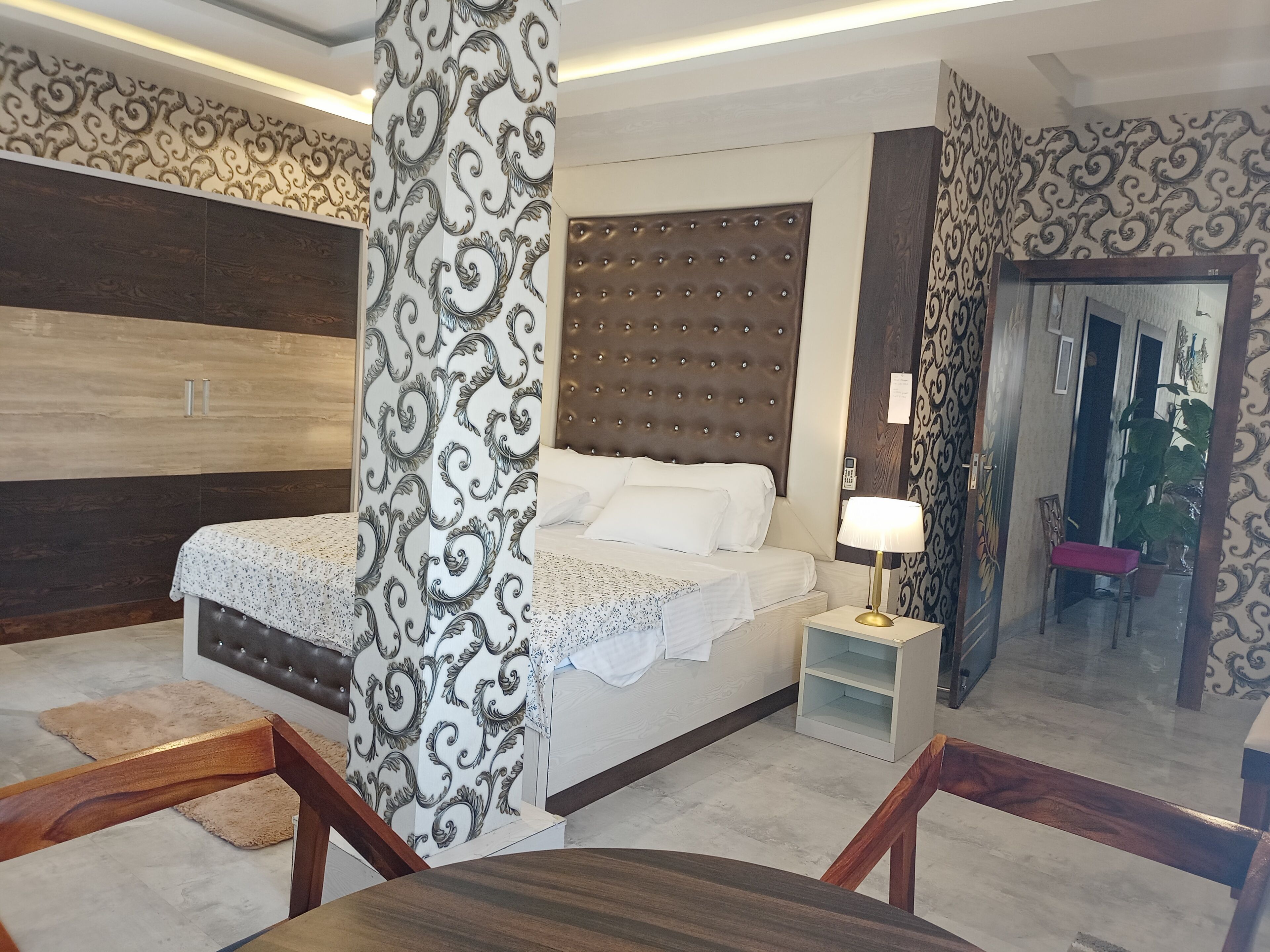 A modern bedroom with a tufted headboard, a large bed with white linens, a bedside table with a lamp, and a wooden chair.