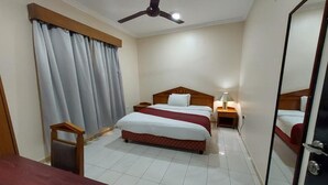 Quarto de hotel com duas camas, um ventilador de teto, uma mesa e um espelho.